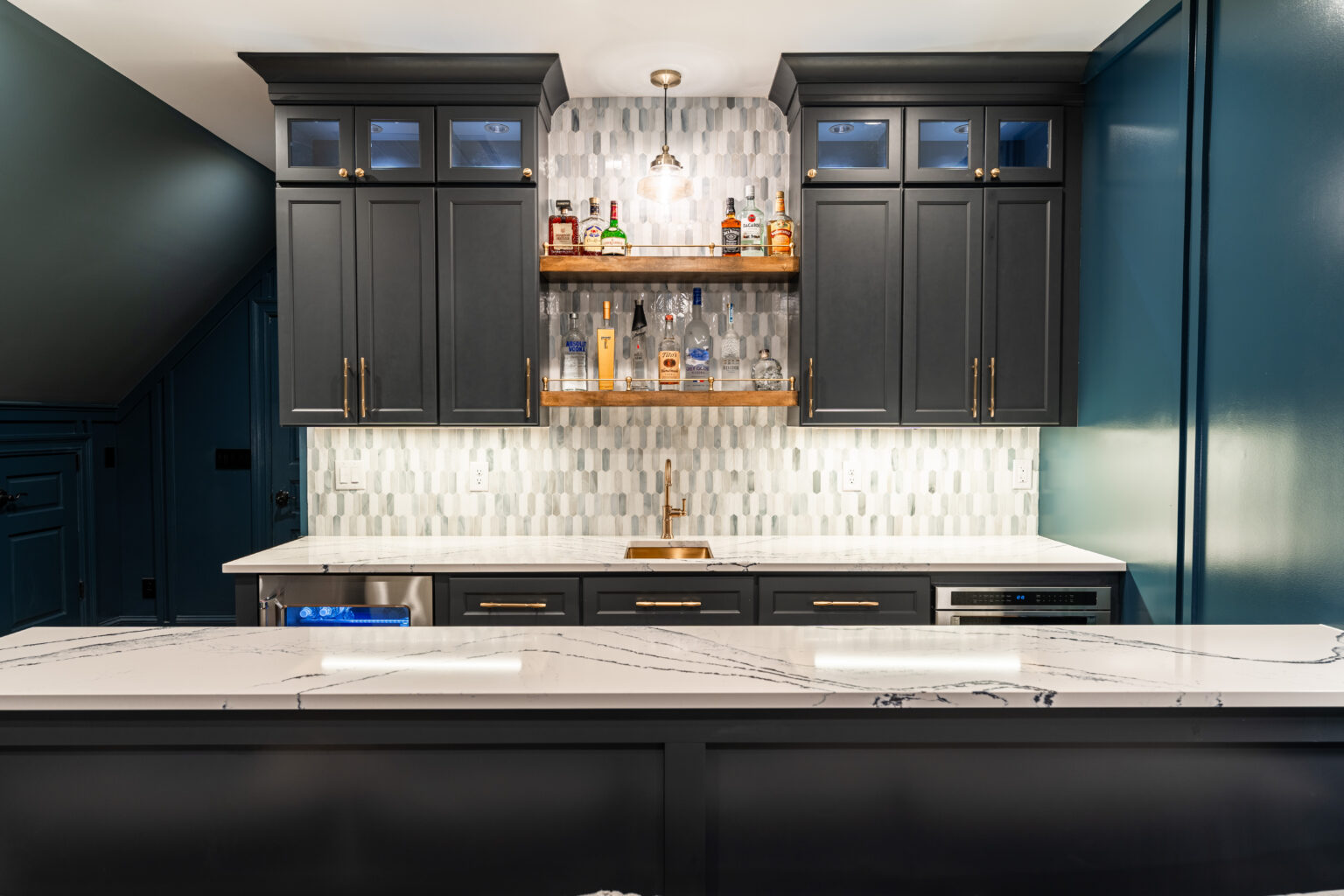 Custom wet bar with charcoal cabinetry, marble counters and a brass sink