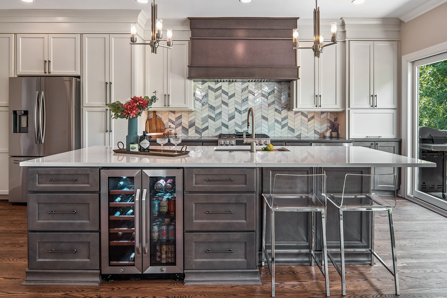 Open kitchen with a grey island, chevron tile backsplash and a timber hood