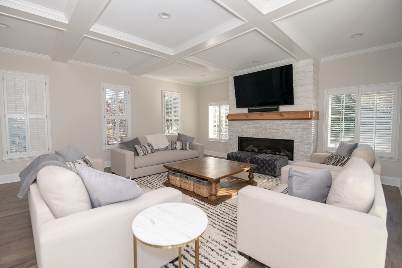 Renovated living room with a coffered ceiling, stone fireplace and plantation shutters
