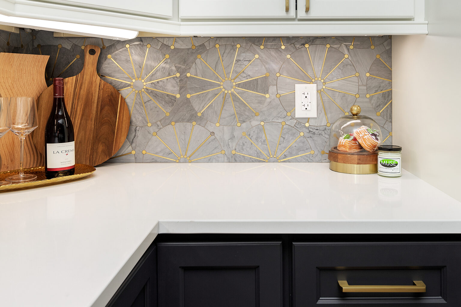 Charcoal kitchen cabinetry with white quartz counters and a marble and brass sunburst tile backsplash